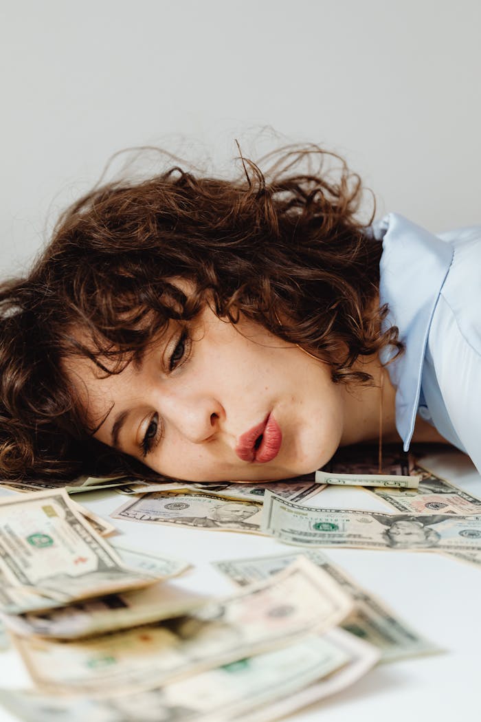 Close-up of a curly-haired woman resting on US dollar bills, conveying financial contemplation.